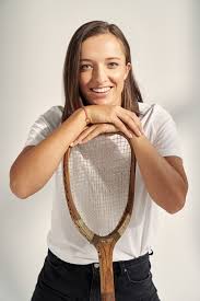 Female tennis player smiling brightly with her chin resting on a tennis racket