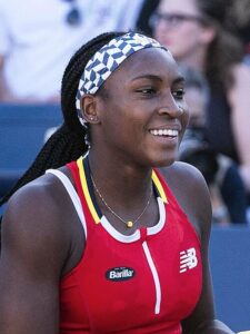 Female tennis athlete sitting on court and smiling cheerfully after practice