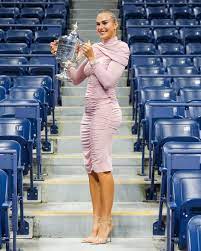 Female tennis champion in a pink dress holding a trophy and smiling with joy